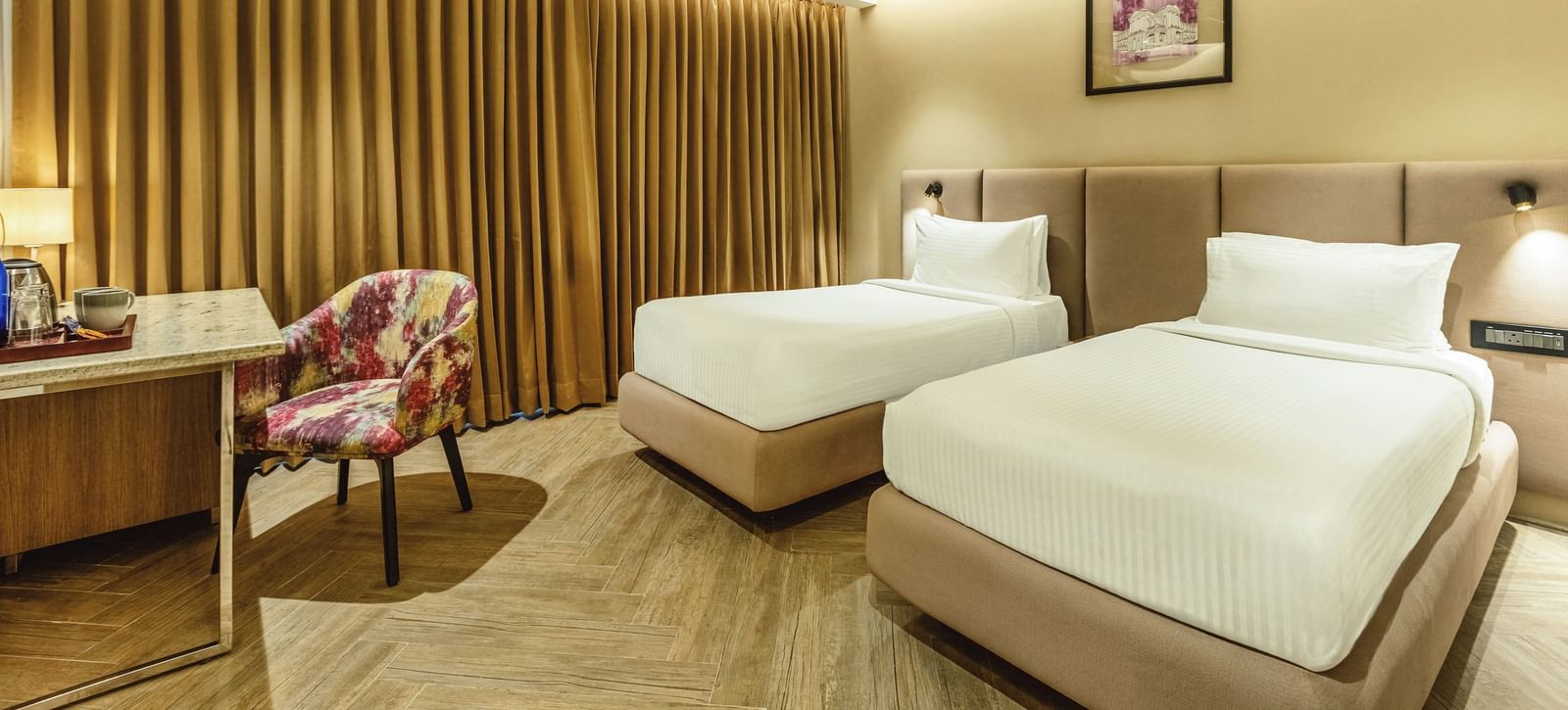A wide shot of a twin-bedded room at Mango Hill Central, Chennai. A desk is on the left, and a wooden slat wall is behind the beds.