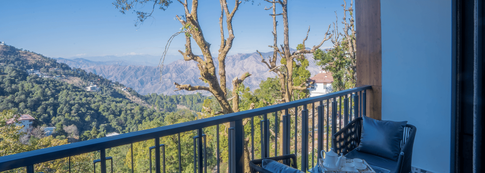 The private balcony at the Executive Room With Balcony & Valley View overlooking a lush green landscape on a bright day at Perfectstayz Premium Westend Mall Road, Mussoorie.