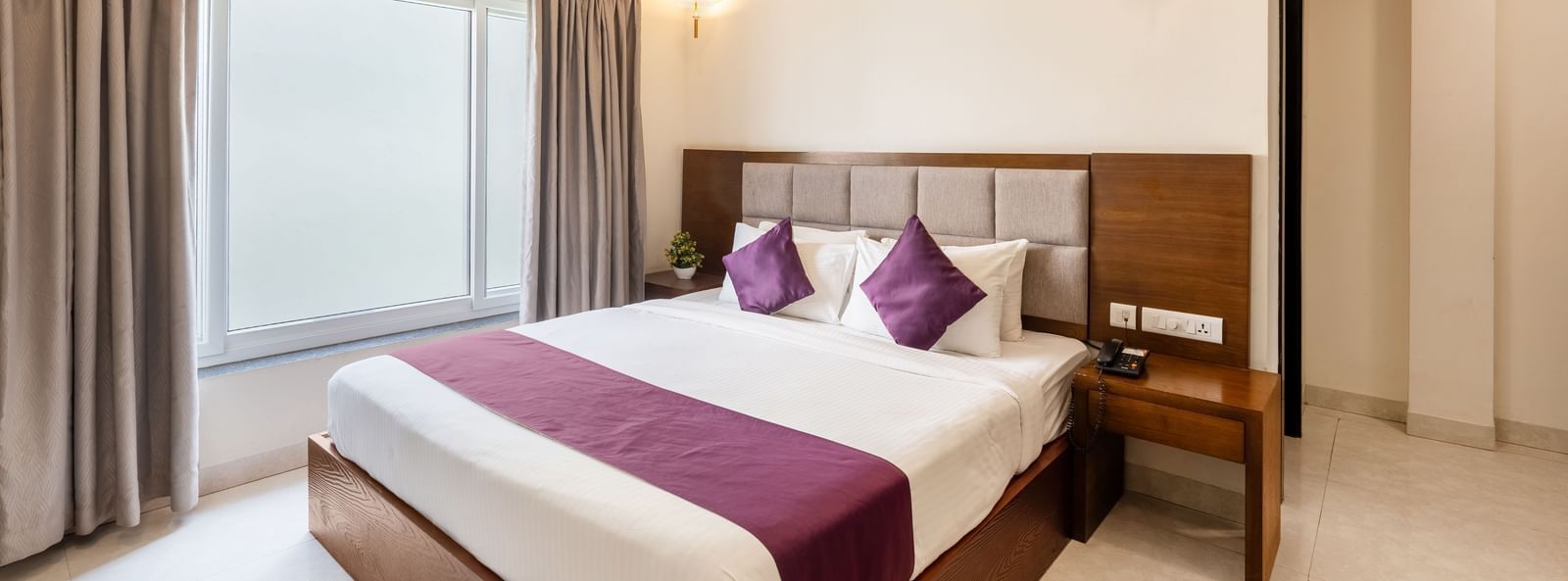A Premium Room at Destino by Monday Hotels, Gachibowli, with a large double bed with purple accents and a ceiling fan, illuminated by natural light from a large window.