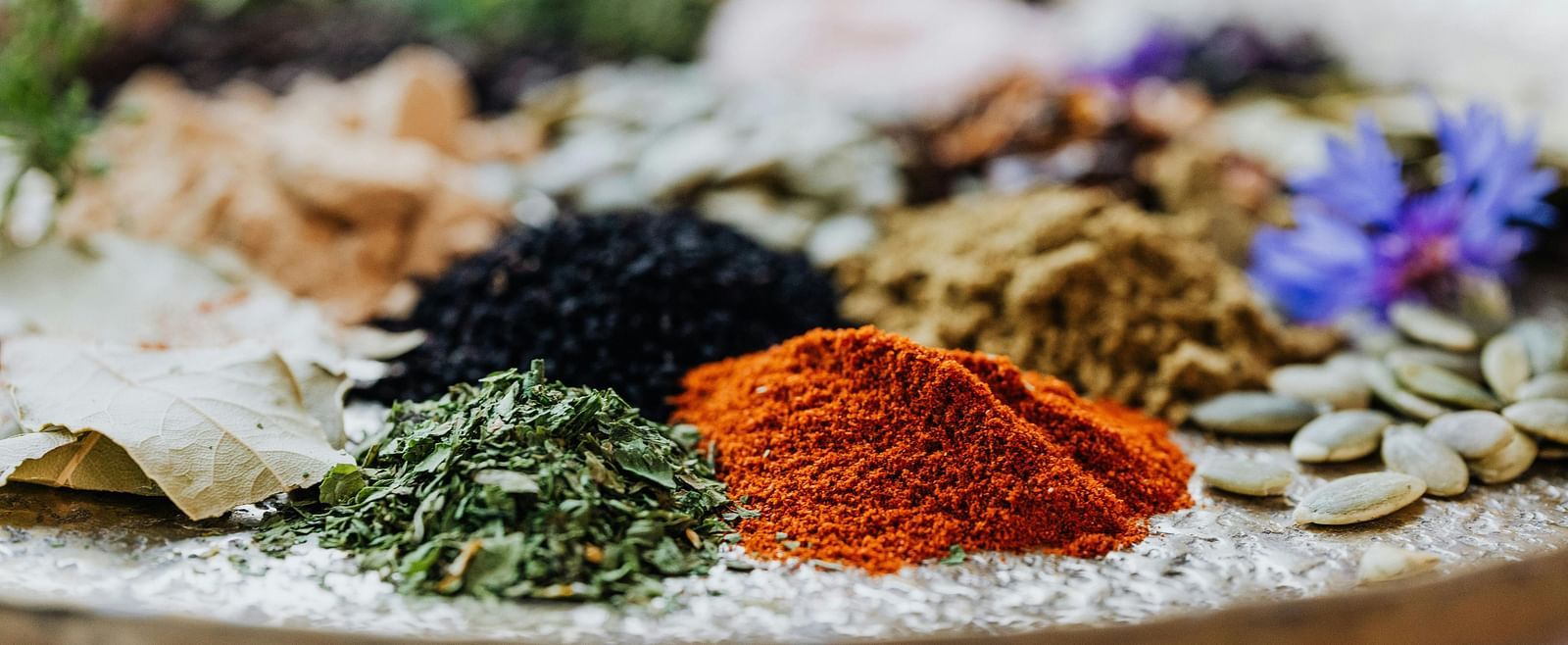  A variety of colorful spices and herbs arranged on a tray, showcasing their natural textures and vibrant colours.