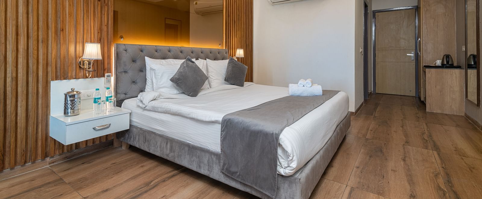 An image of a deluxe room featuring a mirror on the accent wall behind the bed also featuring bed side tables, lamps and other room amenities - DLS Ganga Bliss, Haridwar