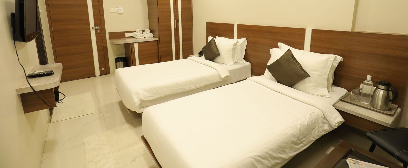 The Super Deluxe Rooms at Highland Resort feature twin beds facing a wall-mounted TV, a wardrobe, a bedside table on which a kettle is placed.