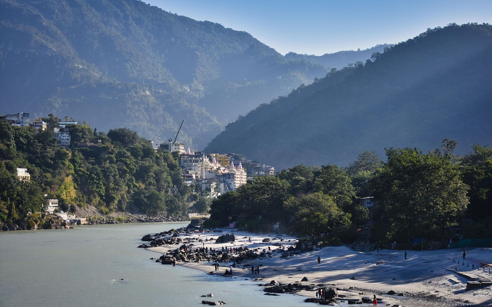 A beautiful landscape featuring the Ganges flowing with lush green mountain ranges in the background.