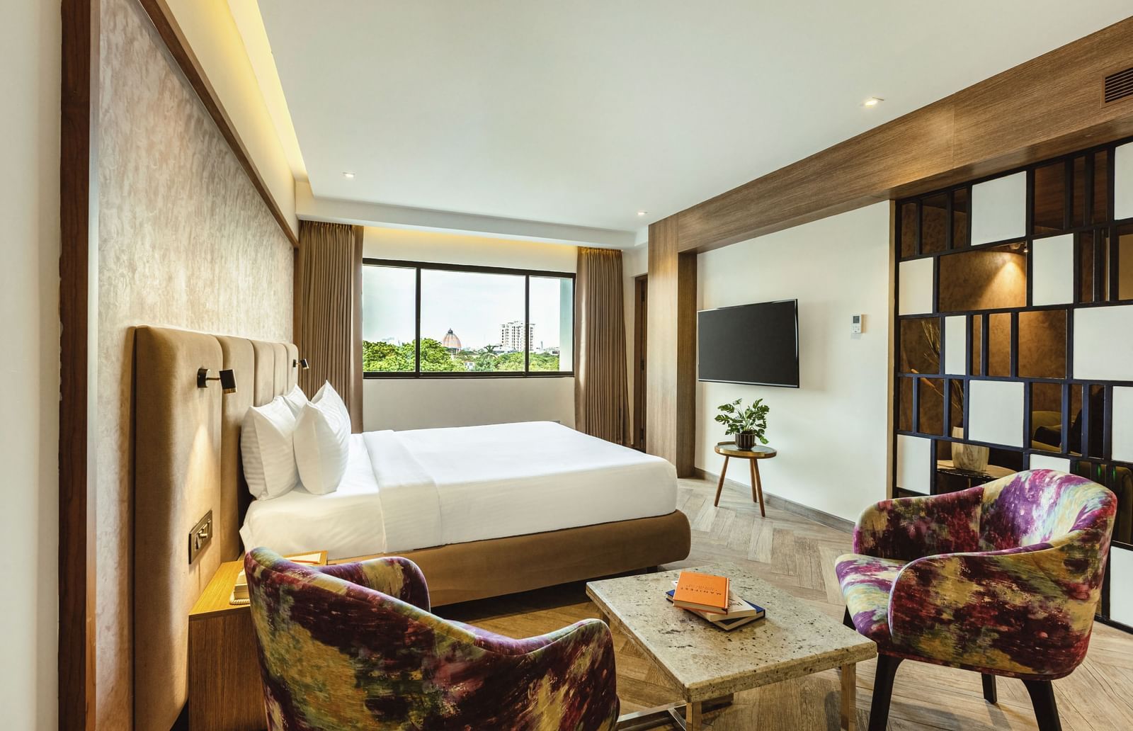 A wide-angle view of a room with a large bed and a seating area at Mango Hill Central, Chennai. A TV is on the far wall.