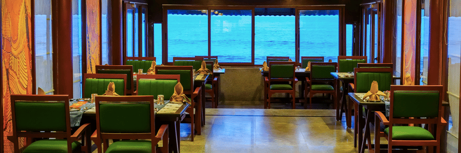 Elegant indoor dining space at MGM Beach Resorts with wooden furniture, ceiling lights, and large windows offering sea views.