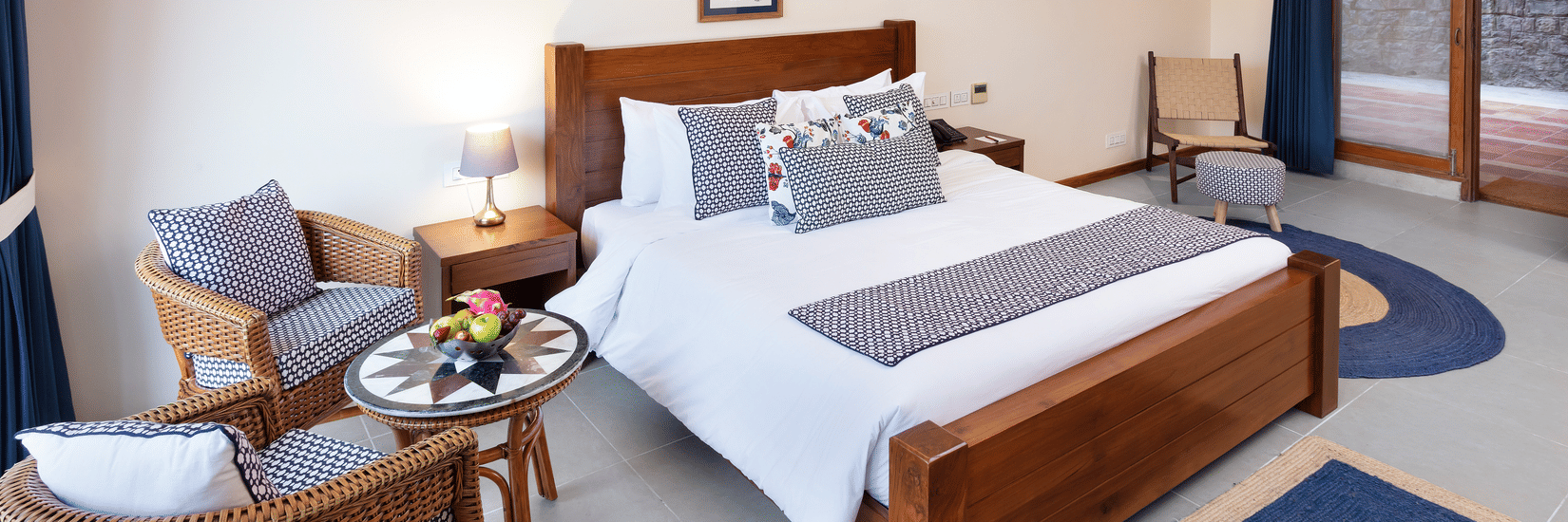 Superior Room at Suryavilas Luxury Resort and Spa featuring a plush bed with a wooden headboard and a lamp on the nightstand next to a seating space for 2 with a coffee table