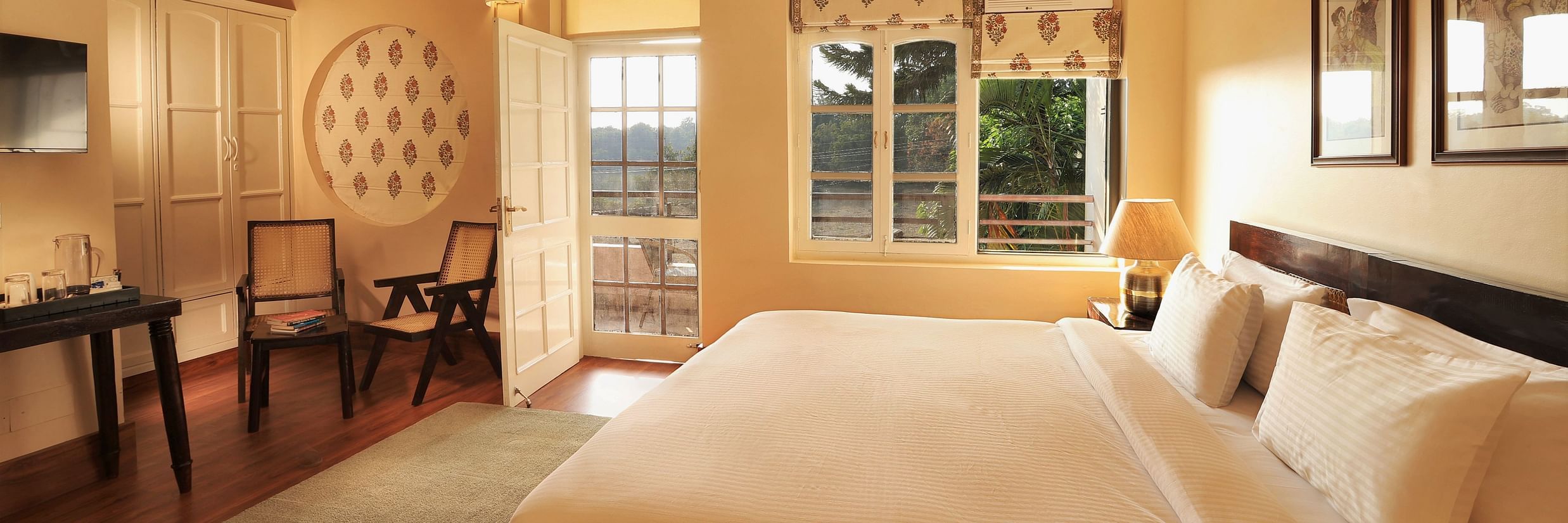 An image of a Super Deluxe Room featuring a double size bed, two chairs, a table where coffee maker is kept, and an open door from where sunlight is flooding the room - Lamrin Boutique Cottages Rishikesh