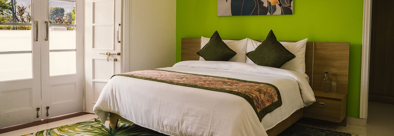 A spacious room at BluSalzz Villas - The Green Roof, Bhimtal featuring a large bed, a photo frame above the headboard, a carpet, and a door leading to the balcony.