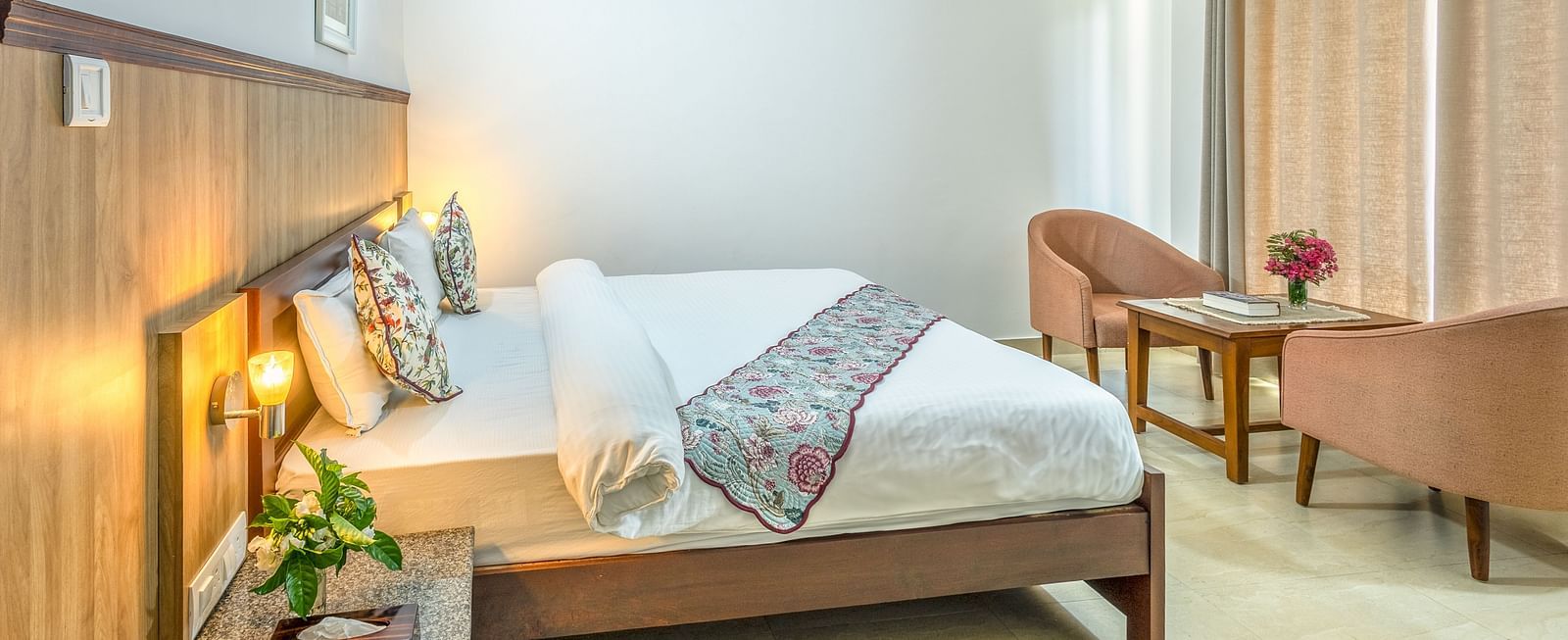 a double bed with side tables, lamps and chairs opposite it inside one of the rooms - Neer ganga Resorts