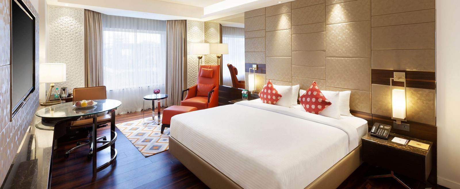 A spacious room with a large bed, wall-mounted TV, table, and cushioned chair, with curtains pulled to the side of the windows | Cenneys Gateway