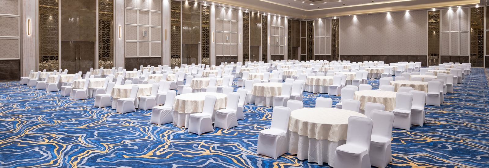 Banquet hall set up with round tables and white linen seating at Merlis Hotel, Coimbatore.