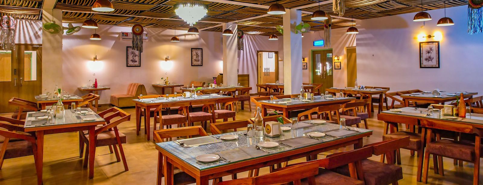 Several set tables and chairs are arranged in a spacious dining hall at Vedikant Resorts The Mallard Corbett.