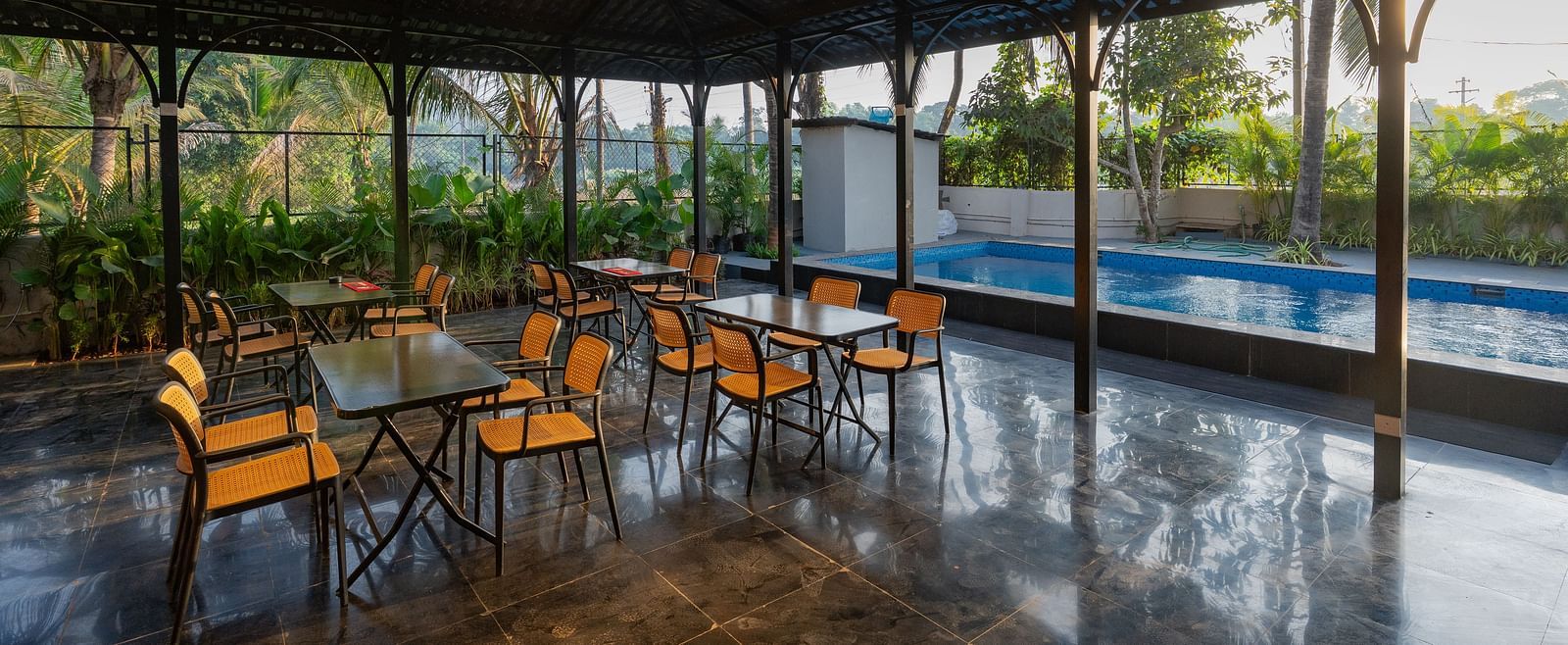 Covered open-air dining area with tables and chairs, overlooking a swimming pool and lush greenery at Kssemya.