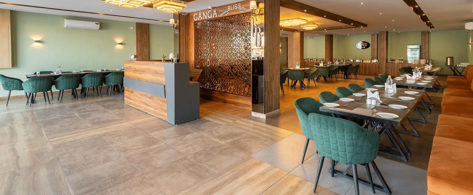 The restaurant image shot from a different angle of DLS Ganga Bliss, Haridwar with chairs, tables and warm lighting