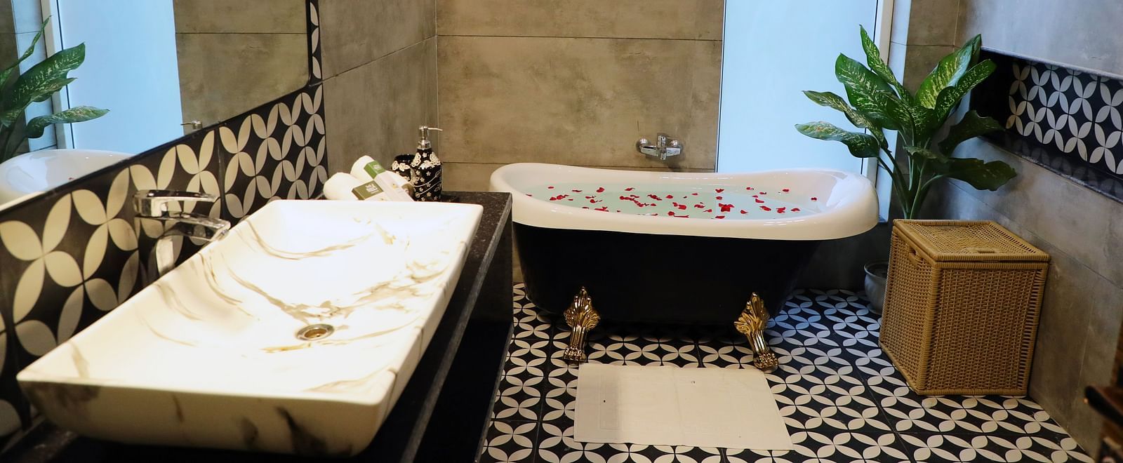 A bathroom at Tisya Farms, Gurgaon with a bathtub, patterned tile floor, two windows, and indoor plants.