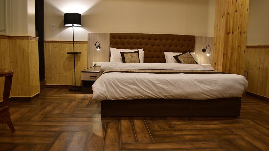 Deluxe Room Apartment Type - lower angle view of a neatly tucked bed with wooden floor and interior and a bedside lamp next - Hotel Montana Vyoo
