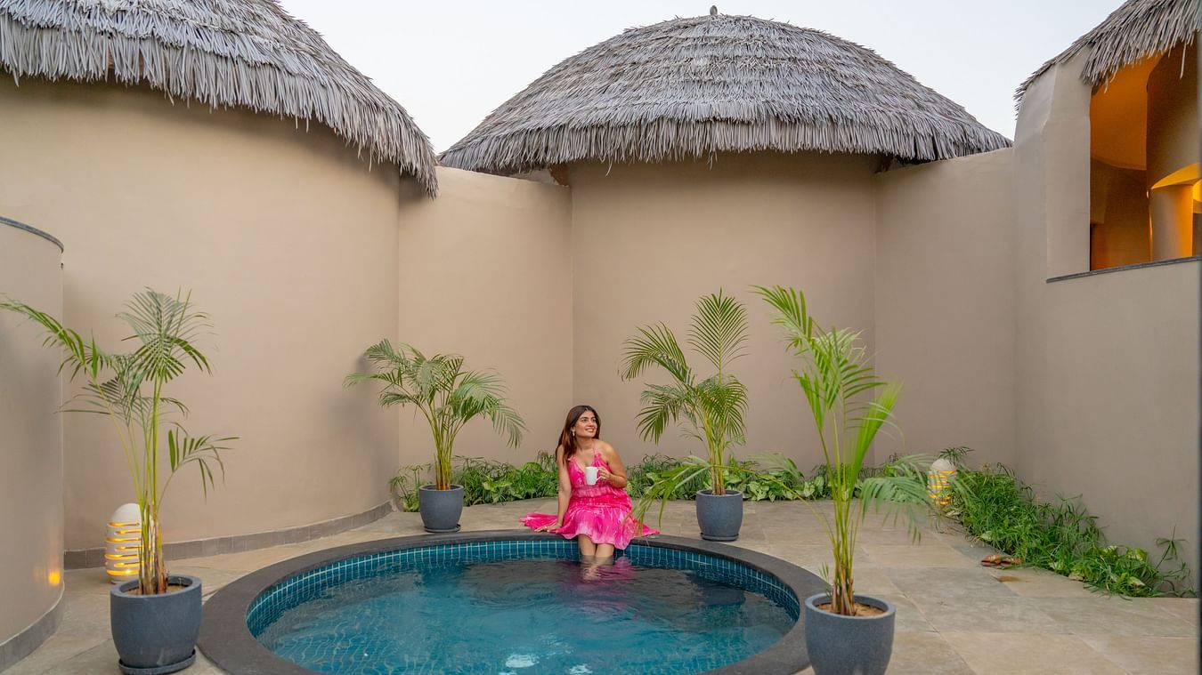 A private plunge pool courtyard with a woman in pink attire, surrounded by thatched-roof cottages at Ananta Spa and Resort, Ajabgarh.