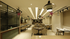 An image of a restaurant with several sets of table and chairs, lights installed on the ceiling, stars hanging from the ceiling, and there is also a counter at one side of the room - Tulip Inn, Zirakpur