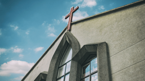 A church building with a cross on the roof against a blue sky with clouds.
