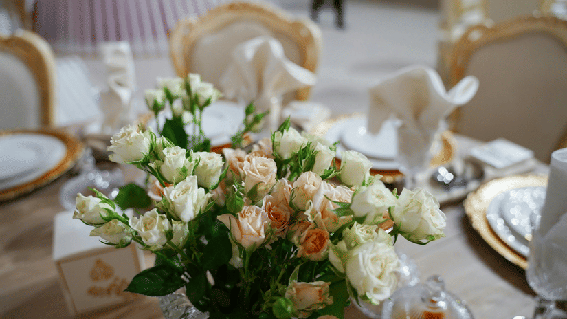 A close up shot of a beautiful flower vase with a lot of white and pink roses on a dining table.