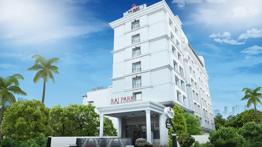 Facade image of Raj Park Hotel, Chennai, with trees on either side and blue sky in the background.