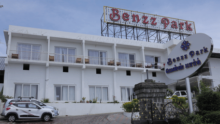Hotel exterior with signage, a paved driveway and parked cars, showcasing a popular Kodaikanal resort for family stays at Benzz Park.