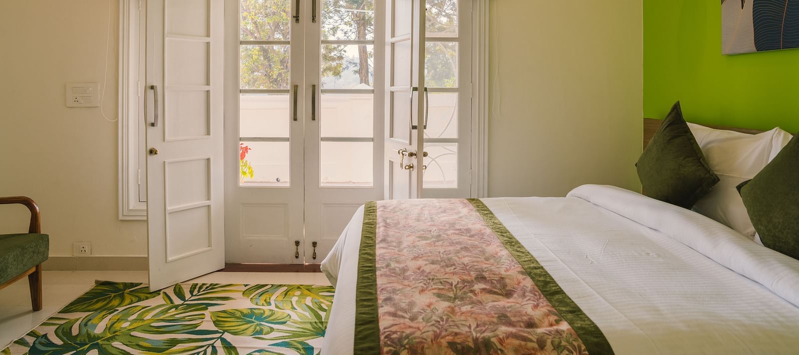 A side view of the neatly made bed with a carpet on the floor and a pair of glass-panel doors leading to the balcony at  BluSalzz Villas - The Green Roof, Bhimtal.