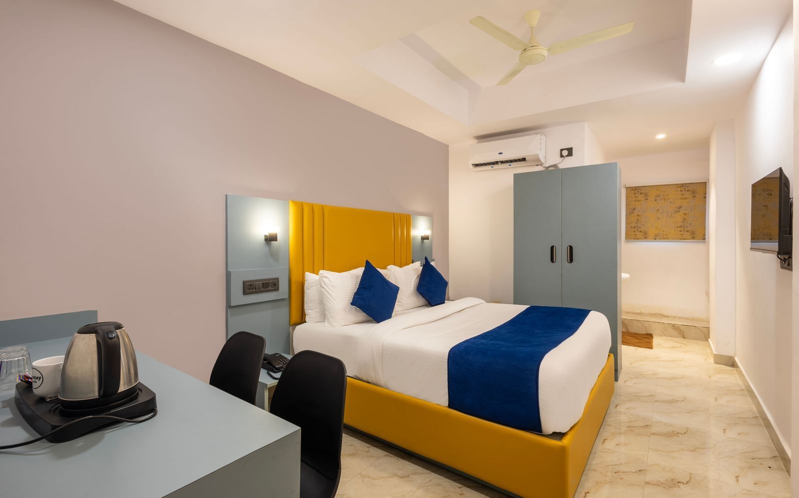 Side view of a Deluxe Room with a bed, blue and white bedding, a yellow headboard, and a desk area - Beestay Hotels Financial District, Hyderabad 
