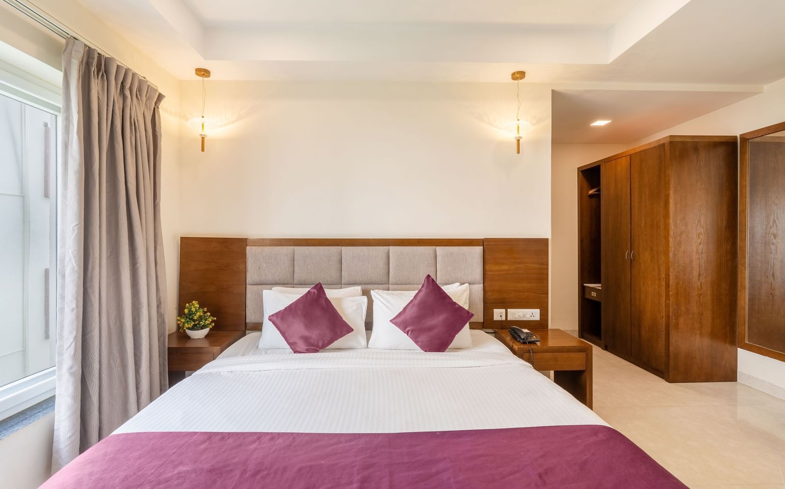 A well-lit room at Destino by Monday Hotels, Gachibowli, featuring a neatly made double bed with purple accents and a spacious wooden wardrobe.