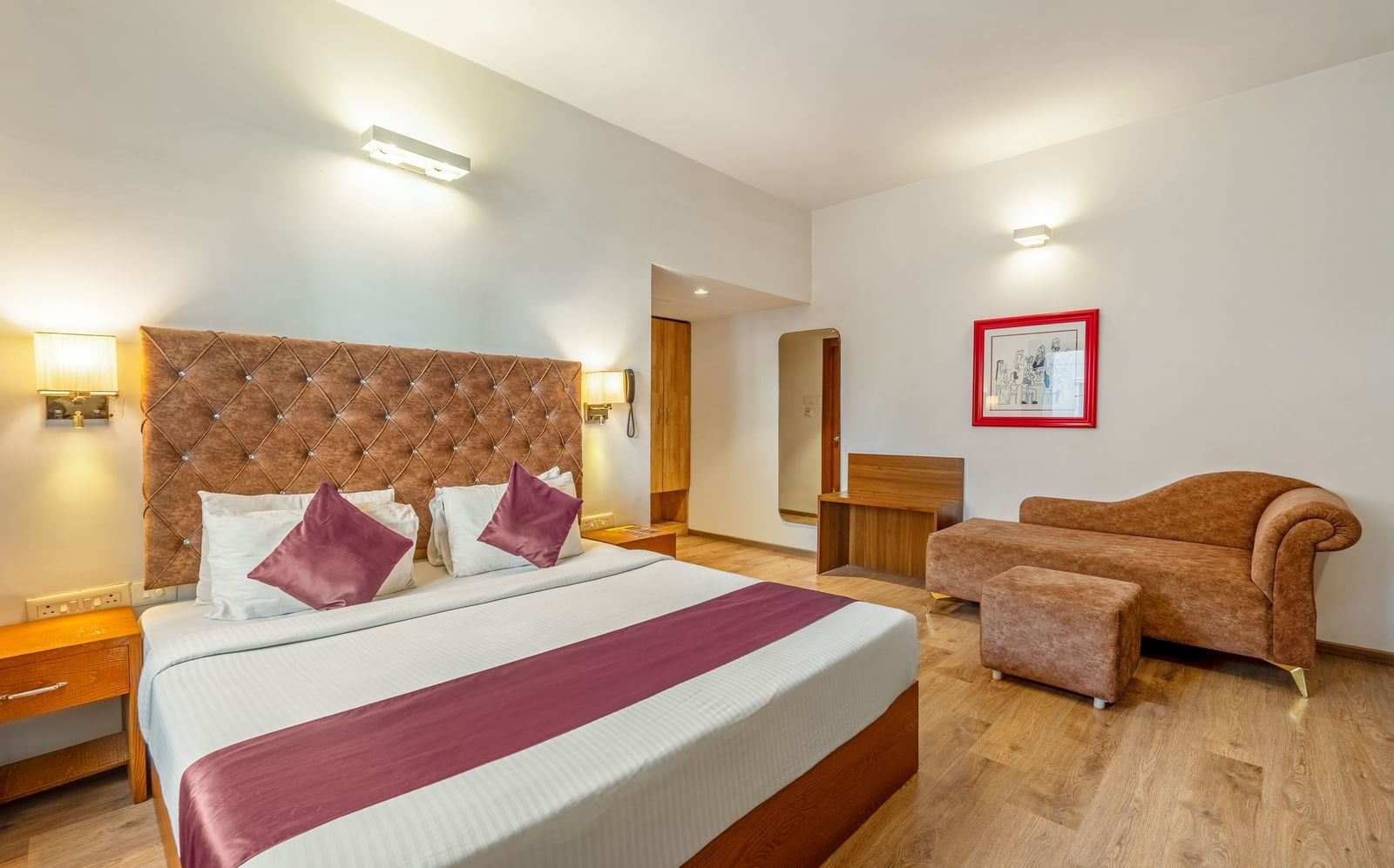 A hotel room with a double bed, a cushioned sofa, and a wooden desk placed beside the bed - Monday Hotels HITEC City, Hyderabad