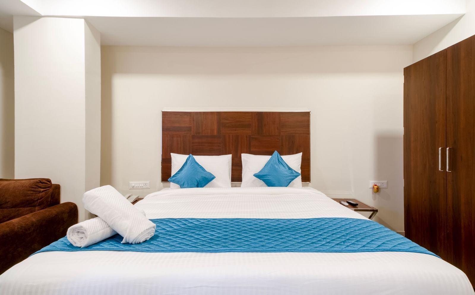 Elegant bedroom with wide bed blue accents soft pillows and wooden wardrobe offering comfort and relaxation at Swarna's The Capital.