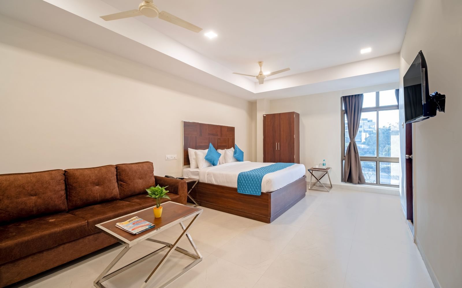 Bedroom with double bed blue decor sofa seating area television and soft lighting for a homely stay at Swarna's The Capital.
