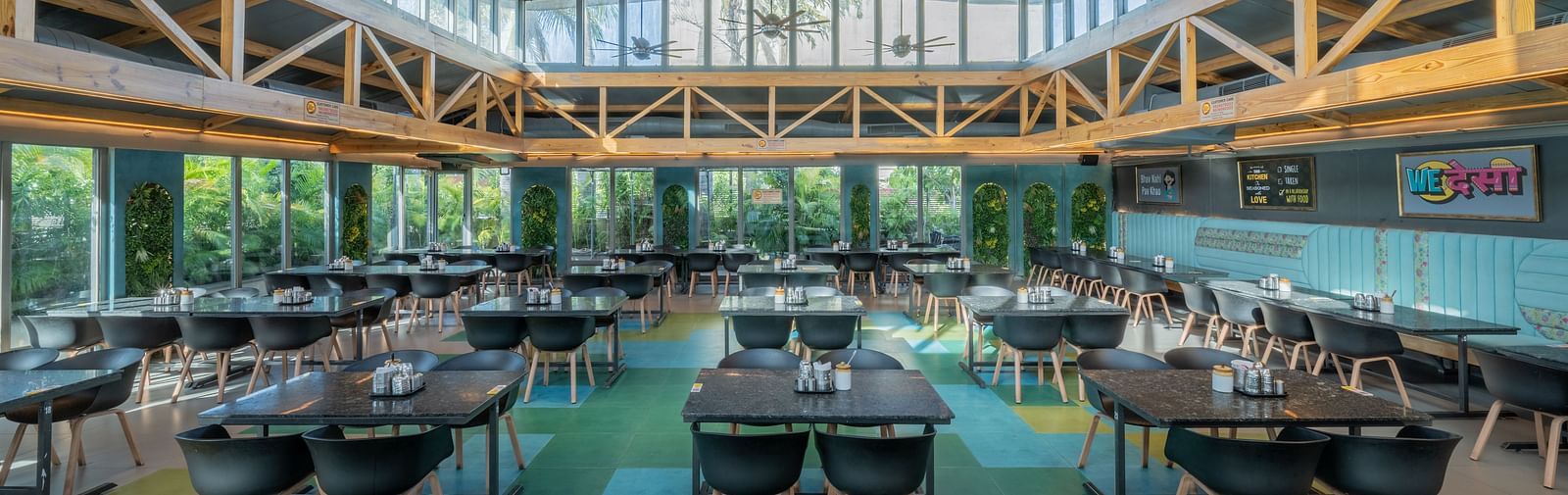 Bright dining area with black chairs, yellow ceiling beams, and large windows at Hotel Highway King, Jaipur.