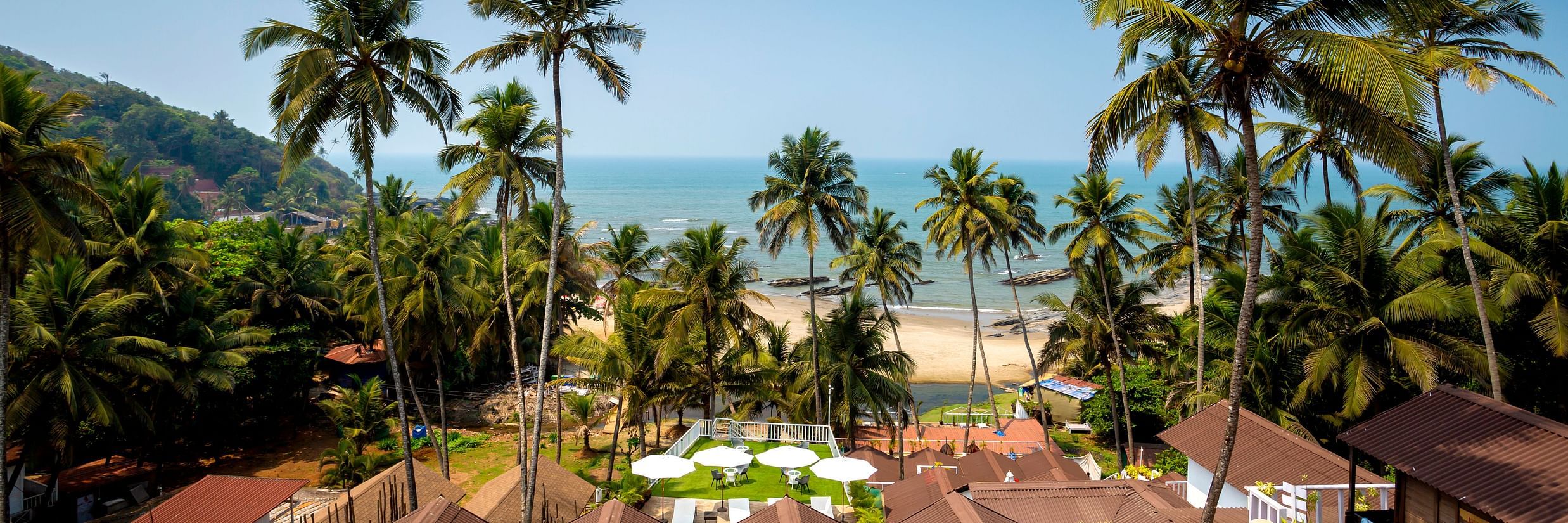 an upper angle view of the sea from cottages at a resort with coconut trees swaying, and shot during the day - Stone Wood Hotels & Resorts