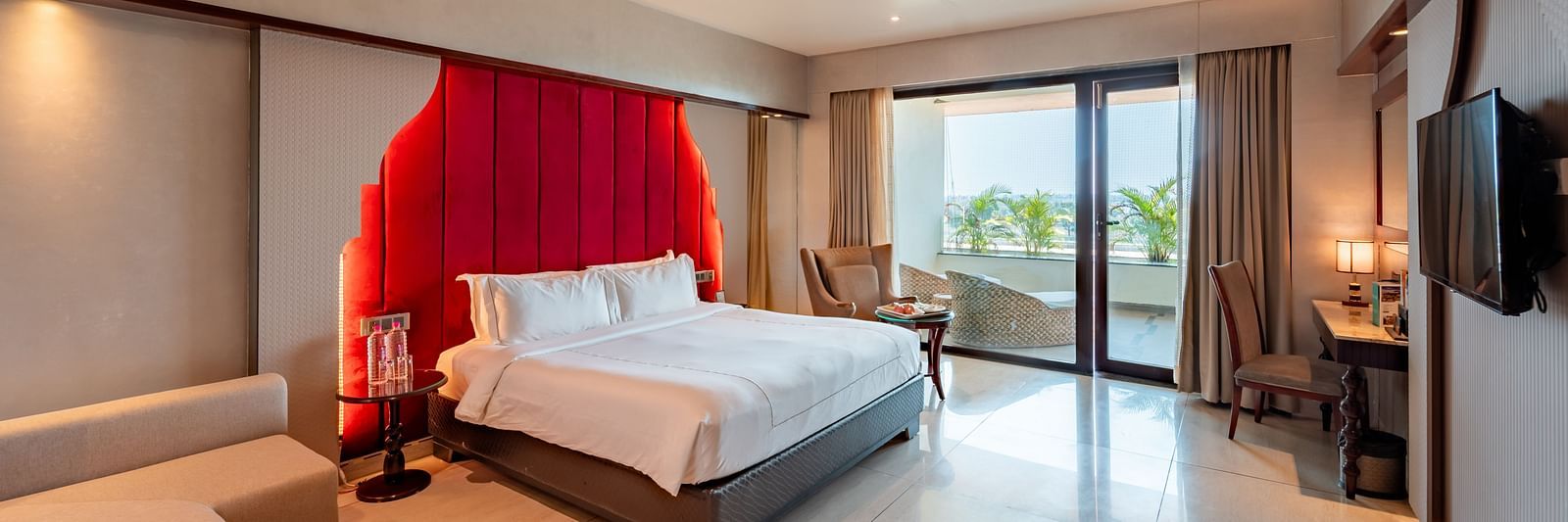 Executive Room features a spacious bed, cushioned sofa, wall-mounted television, and a large doorway leading to the balcony at Crescent Spa & Resort, Indore