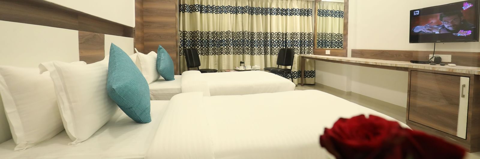 A close-up view of a bed at Imperial Grande with white bedding and a red rose placed near it.