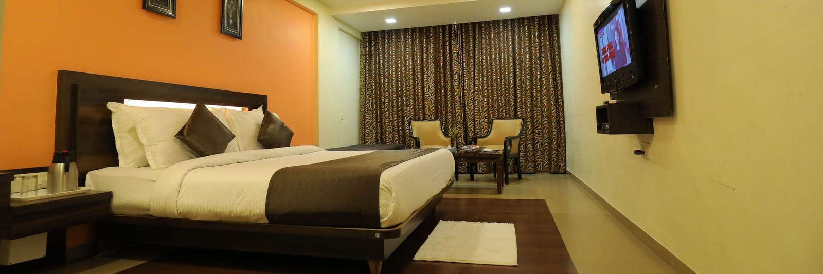 A spacious bedroom at Krushnai Resort with a bed, an orange wall, and a large TV mounted on the wall.