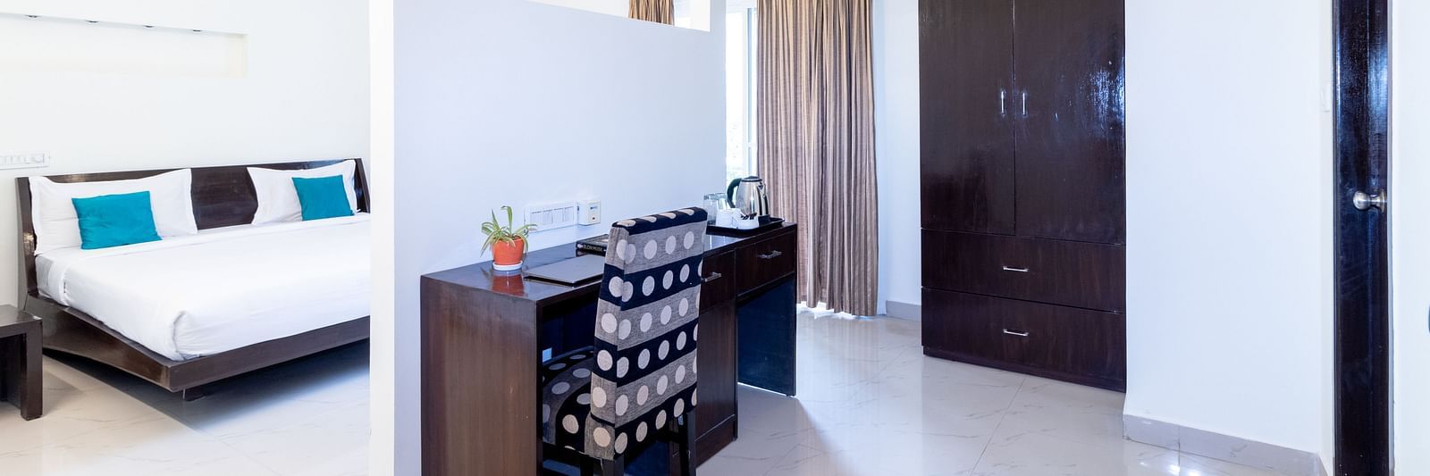 A room shows a double bed in one area and a dining table with chairs in another at Sanctum Suites Domlur, Bangalore.
