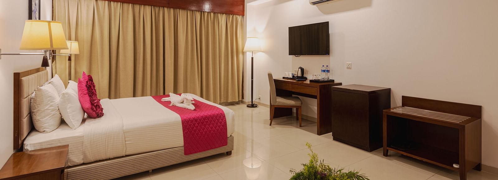 Comfortable hotel room at Diamond Palace Lords Plaza with a double bed, work desk, mounted TV, and a seating area.