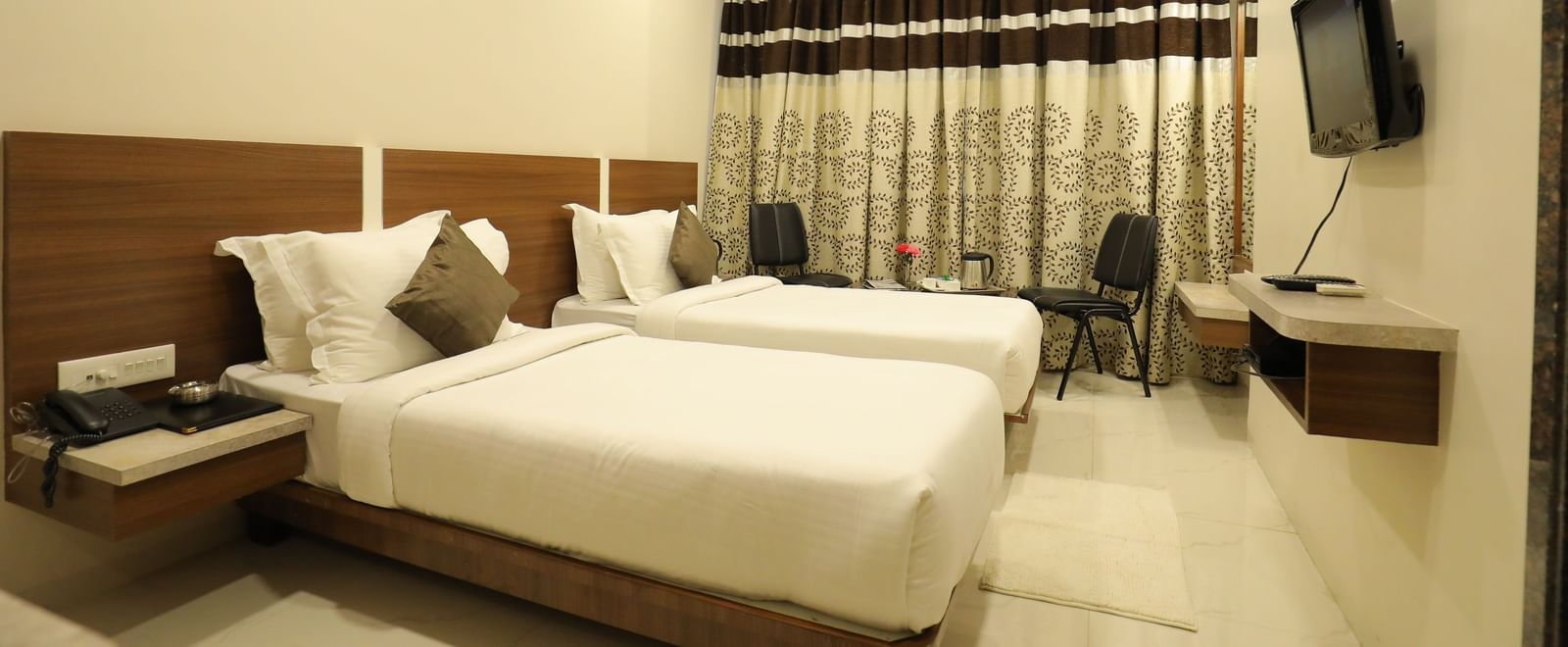 A Super Deluxe Room of Highland Resort furnished with twin beds, a wall-mounted TV, seating area for two, and closed curtains.