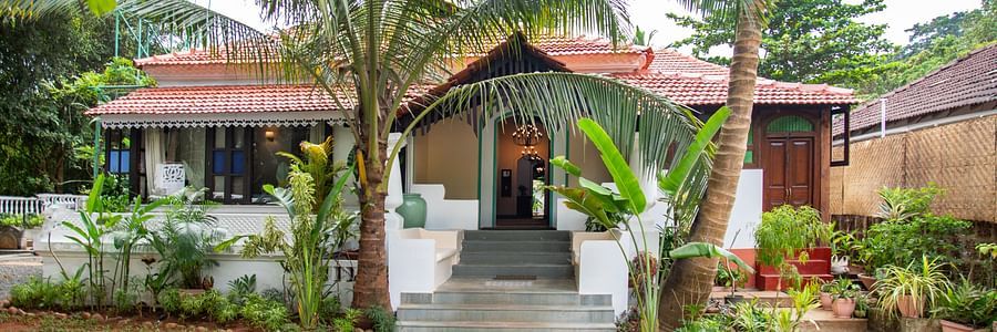 An image of a cottage style bungalow at Lamrin Ucassaim Hotel, Goa which is surrounded by palm trees