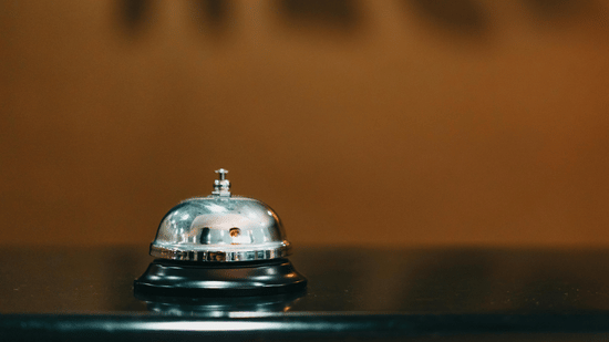 A hand bell places on a counter, with blurred image of writing on a wall.