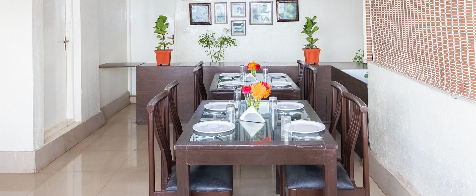 A dining area with a wooden table, chairs, and decorated with framed pictures and potted plants at Sanctum Suites Domlur, Bangalore.