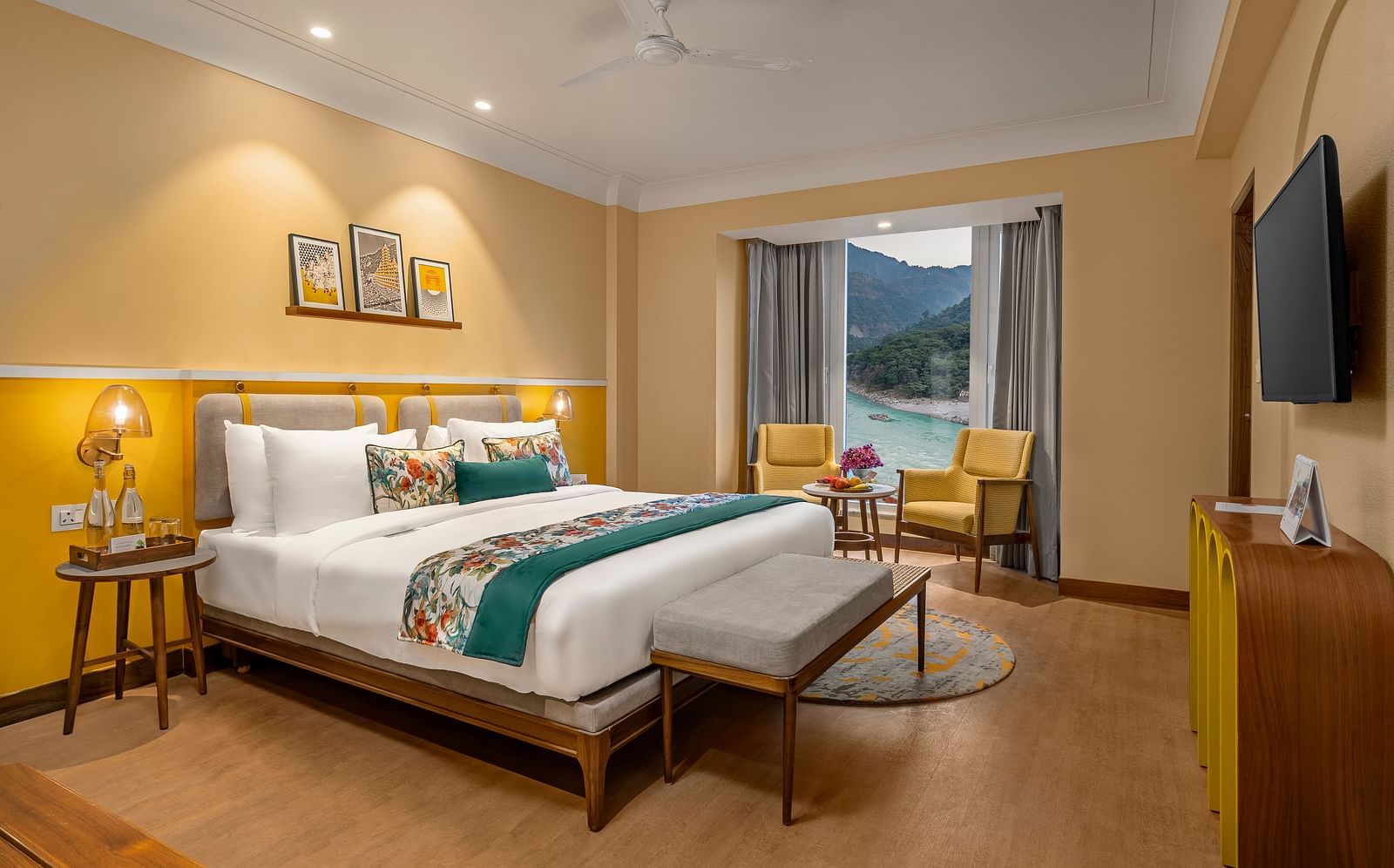  The room features a king-size bed with a plush headboard and comofrtable bedding. Armchairs by the window, offering a scenic view of the mountains. The room also includes a wooden desk, a television, and a ceiling fan. 
