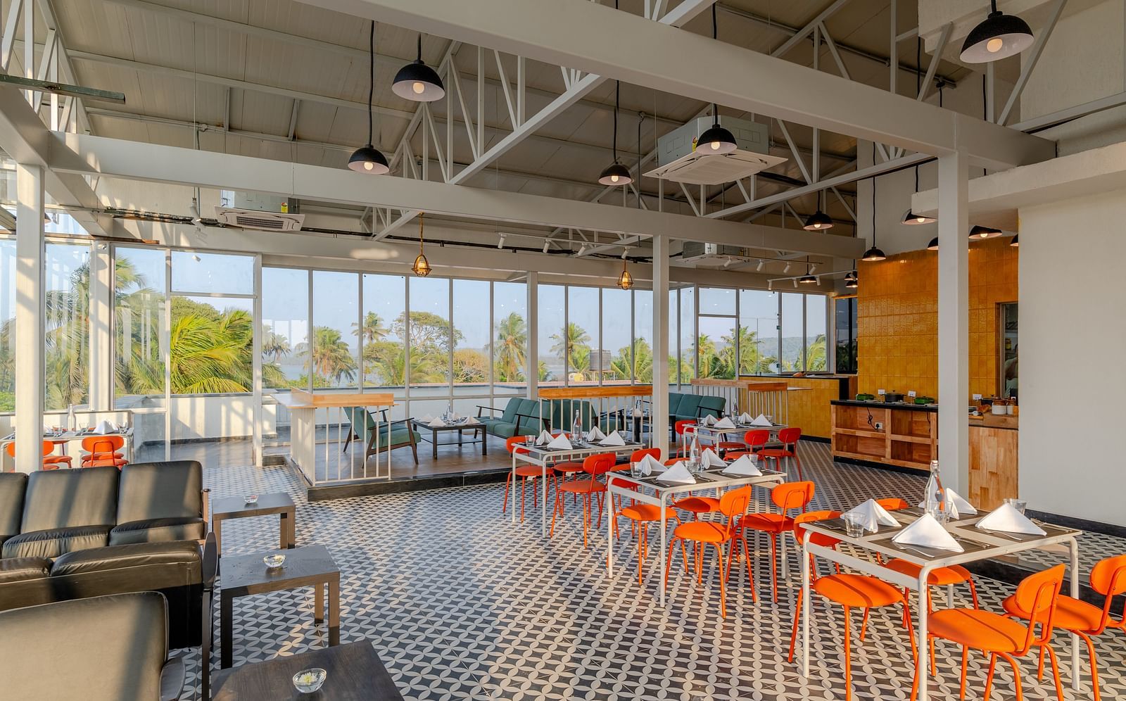  spacious and airy restaurant with industrial-style exposed ceiling, large windows letting in natural light, and a color palette of orange and grey, providing a relaxed dining atmosphere  at Bedzzz Xclusiv Morjim, Goa
