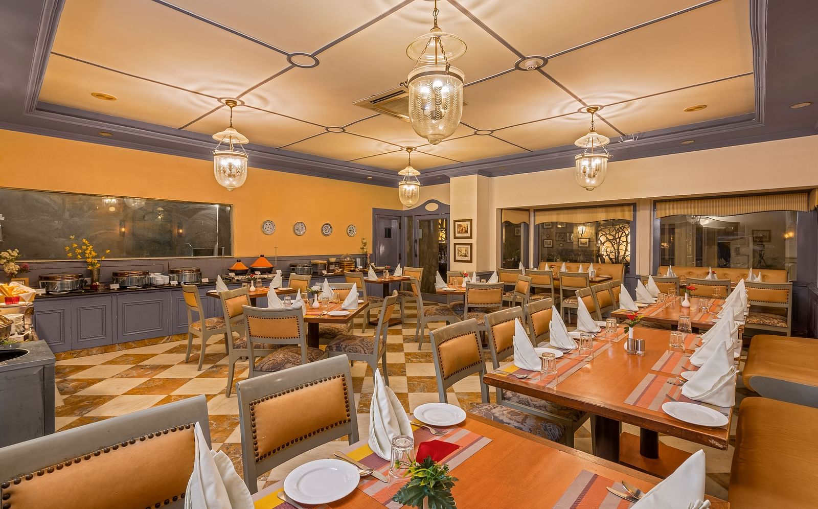 a view of a restaurant with a buffet setting and clusters of tables and chairs with lighting from four chandeliers - The Manor, Kashipur