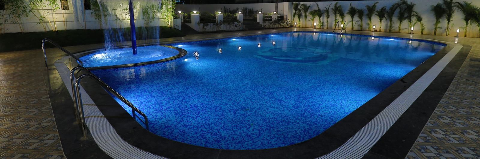 A large swimming pool at Imperial Grande, illuminated with blue lights at night, surrounded by a paved area and some seating.