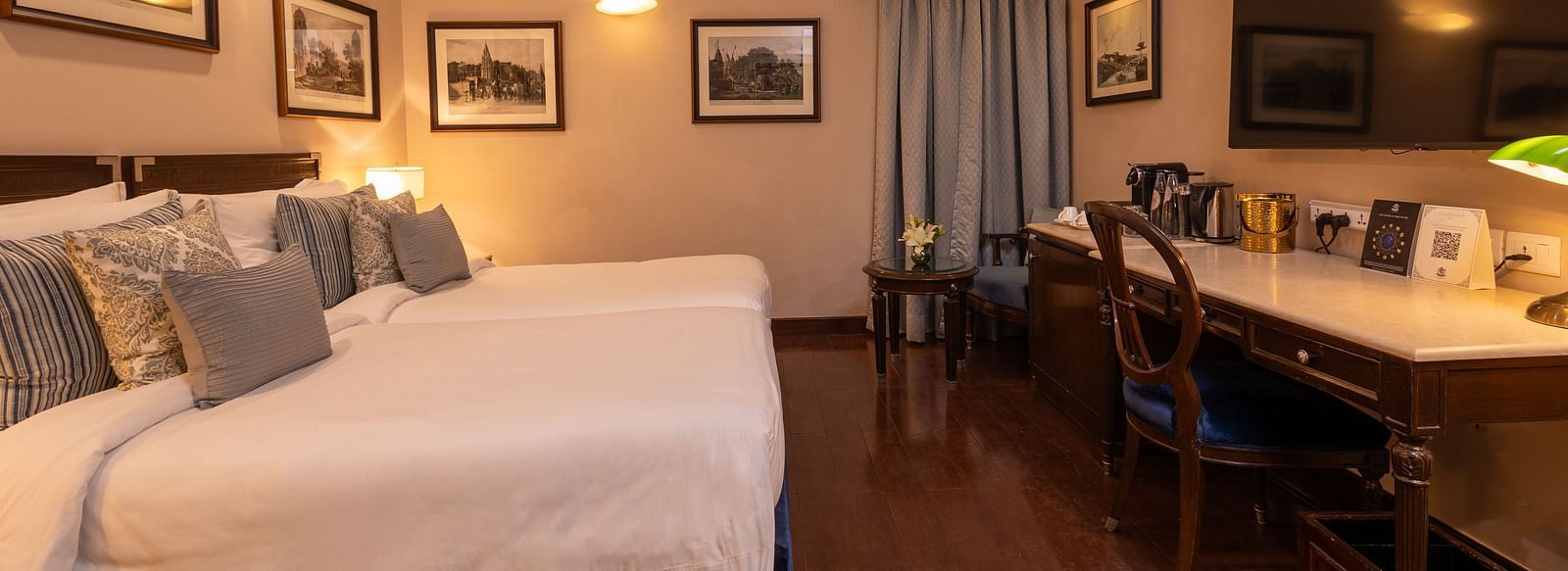 Side view of the Superior Twin Bed Room at The Claridges New Delhi, showcasing twin beds, a wall-mounted TV, and bedside lamps