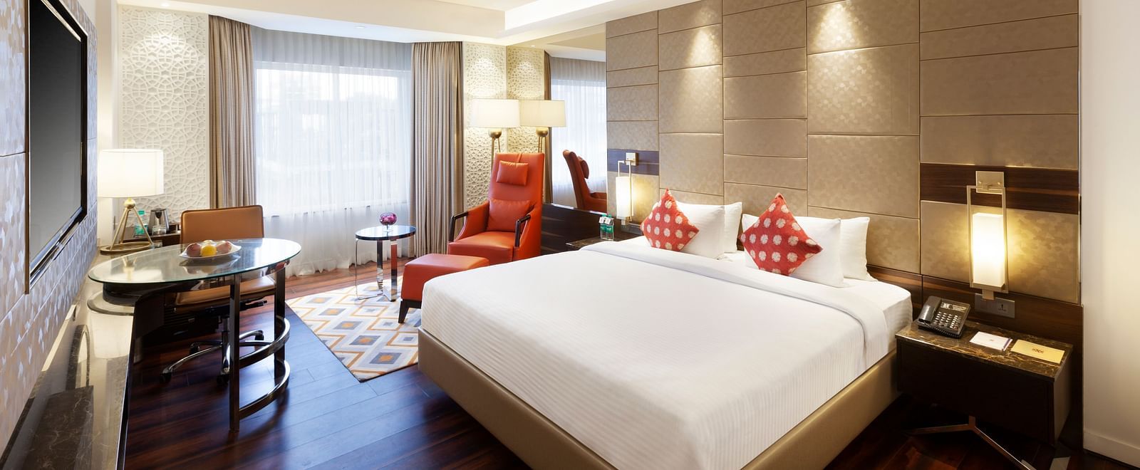 A spacious room with a large bed, wall-mounted TV, table, and cushioned chair, with curtains pulled to the side of the windows | Cenneys Gateway