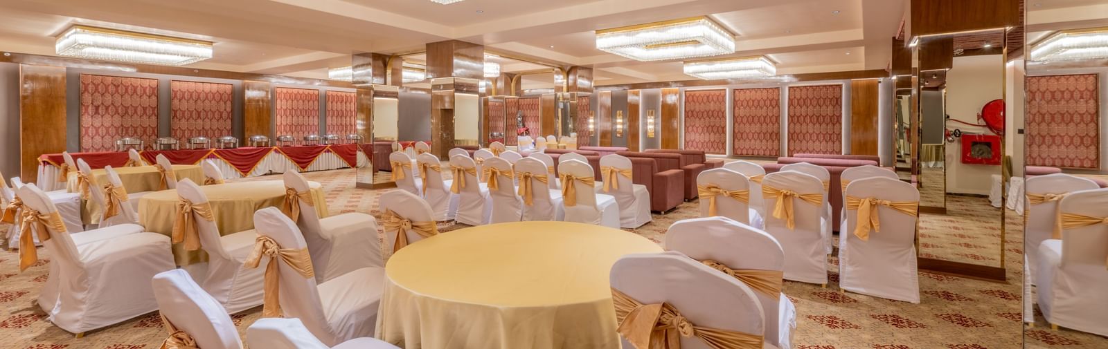 Round tables with yellow tablecloths and white chairs arranged under a decorative ceiling light at Hotel Highway King, Jaipur.